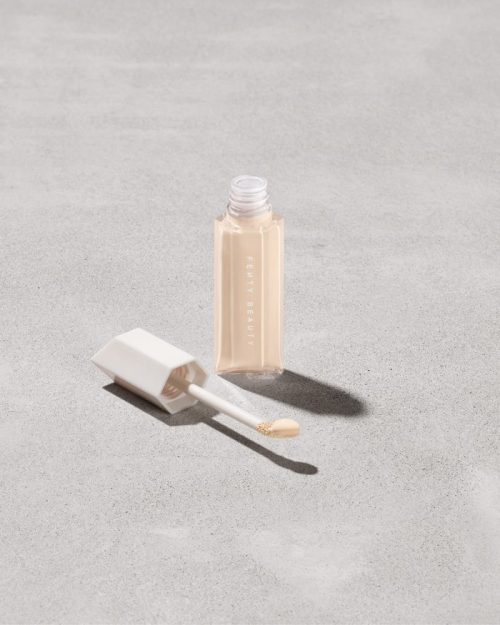 Open bottle of Fenty Beauty We're Even Hydrating Longwear Concealer with doe foot applicator in shade 120n on a concrete background.