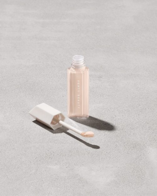 Open bottle of Fenty Beauty We're Even Hydrating Longwear Concealer with doe foot applicator in shade 125c on a concrete background.